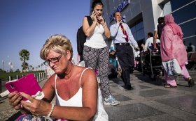 Cindy Crawford from near Glasgow, Scotland, sits on sidewalk away from terminal waiting for more info on a flight on November